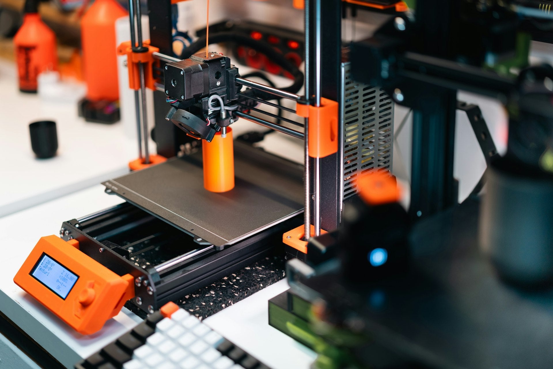 เครื่องพิมพ์ 3D กำลังพิมพ์ชิ้นงานพร็อพสีส้มด้วยเทคนิค FDM สำหรับงานคอสเพลย์